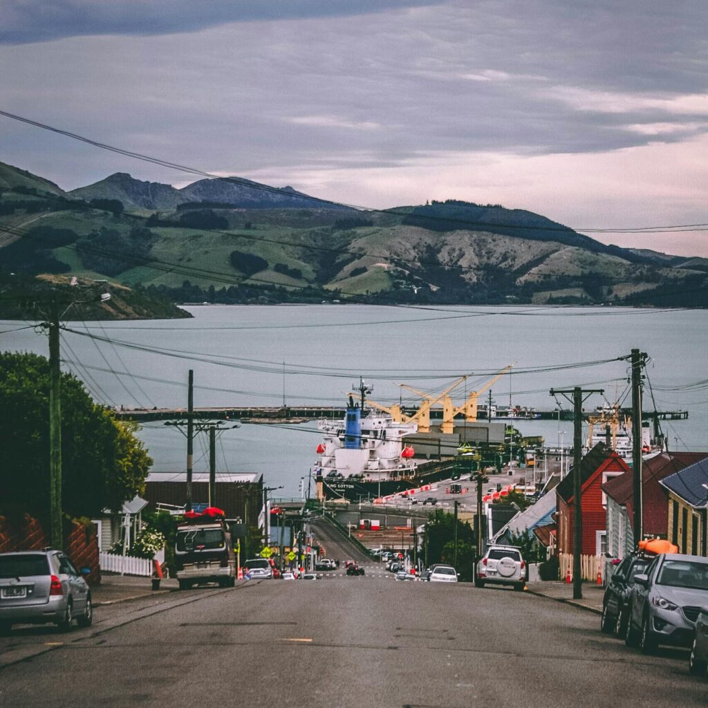 A picturesque street leads to a bustling harbor under cloudy skies, showcasing vibrant coastal life.